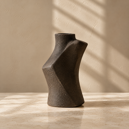 Dark brown textured vase with an angular sculptural silhouette on a sunlit tabletop.
