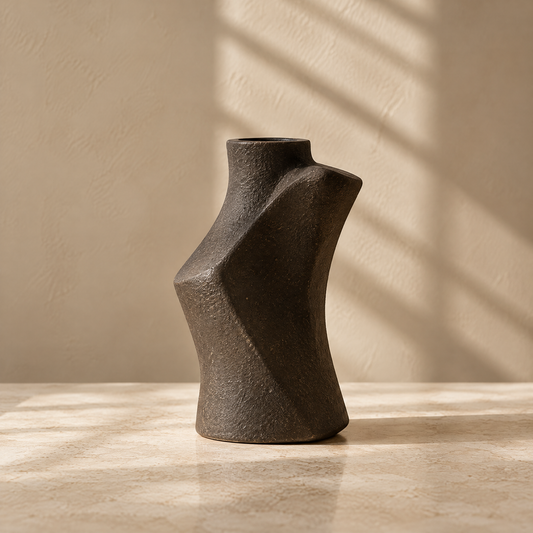Dark brown textured vase with an angular sculptural silhouette on a sunlit tabletop.