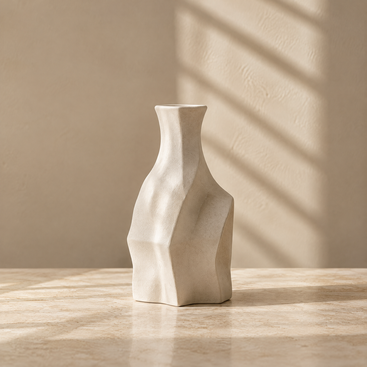Ivory sculptural vase with angular facets and a narrow neck on a sunlit tabletop.